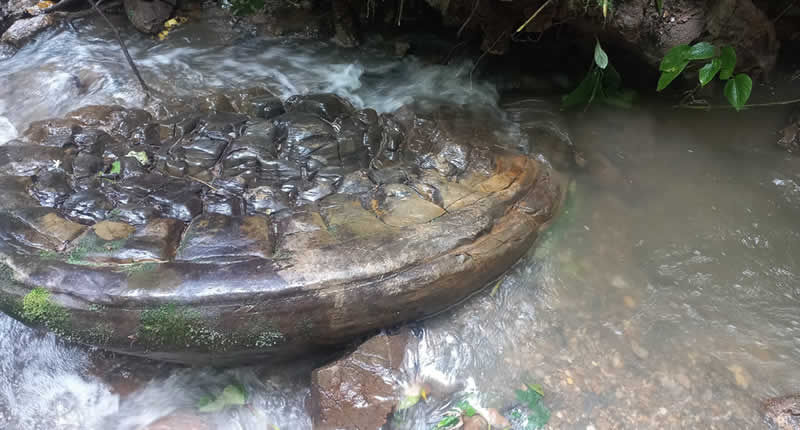 monolithischer Felsblock mit unbekannten Inschriften, in dessen Mitte sich ein geschnitztes Antlitz – ein mythisches Gesicht – abzeichnet